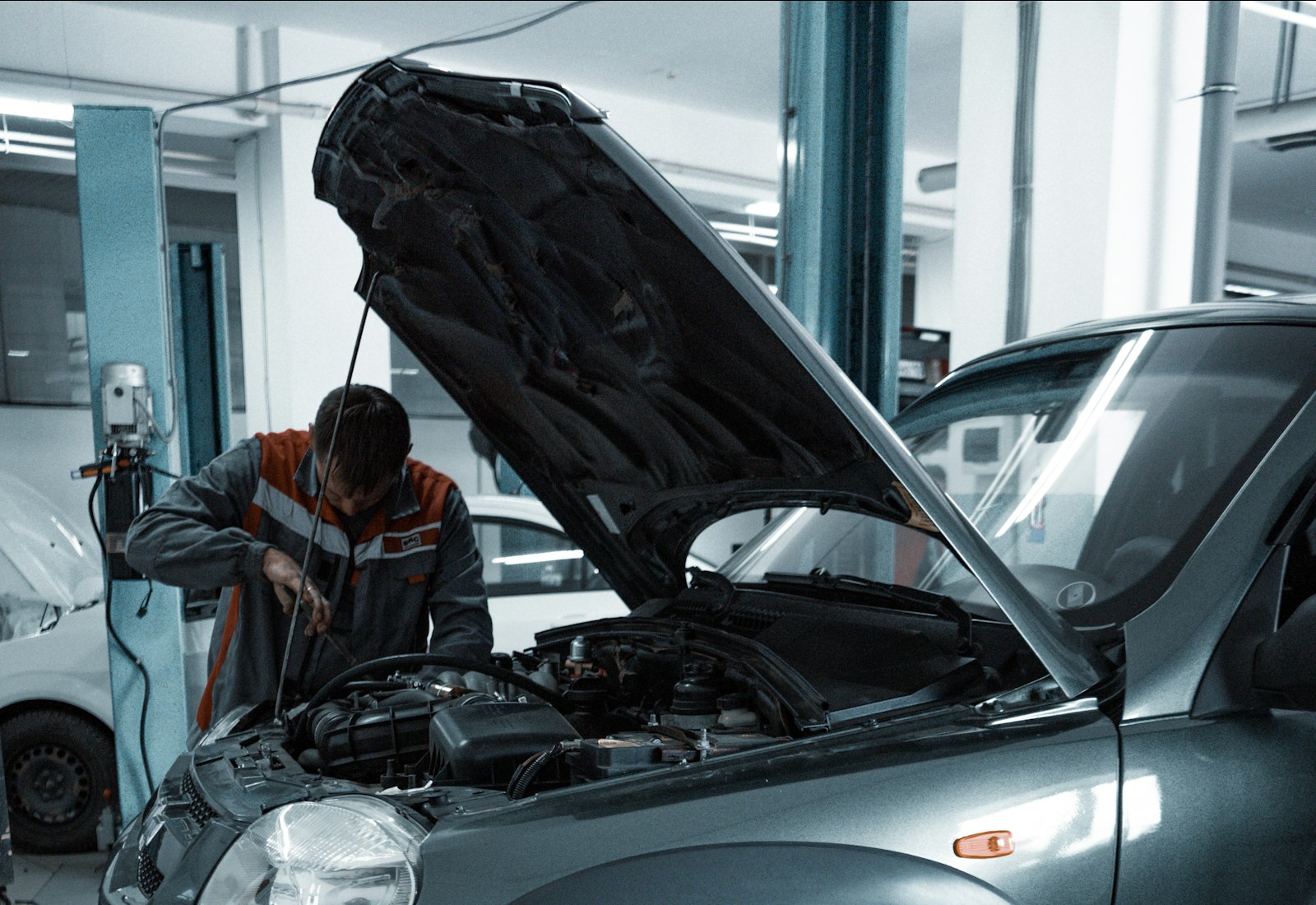 Mechanic in overalls working under a car raised on a hydraulic lift in a busy auto repair garage